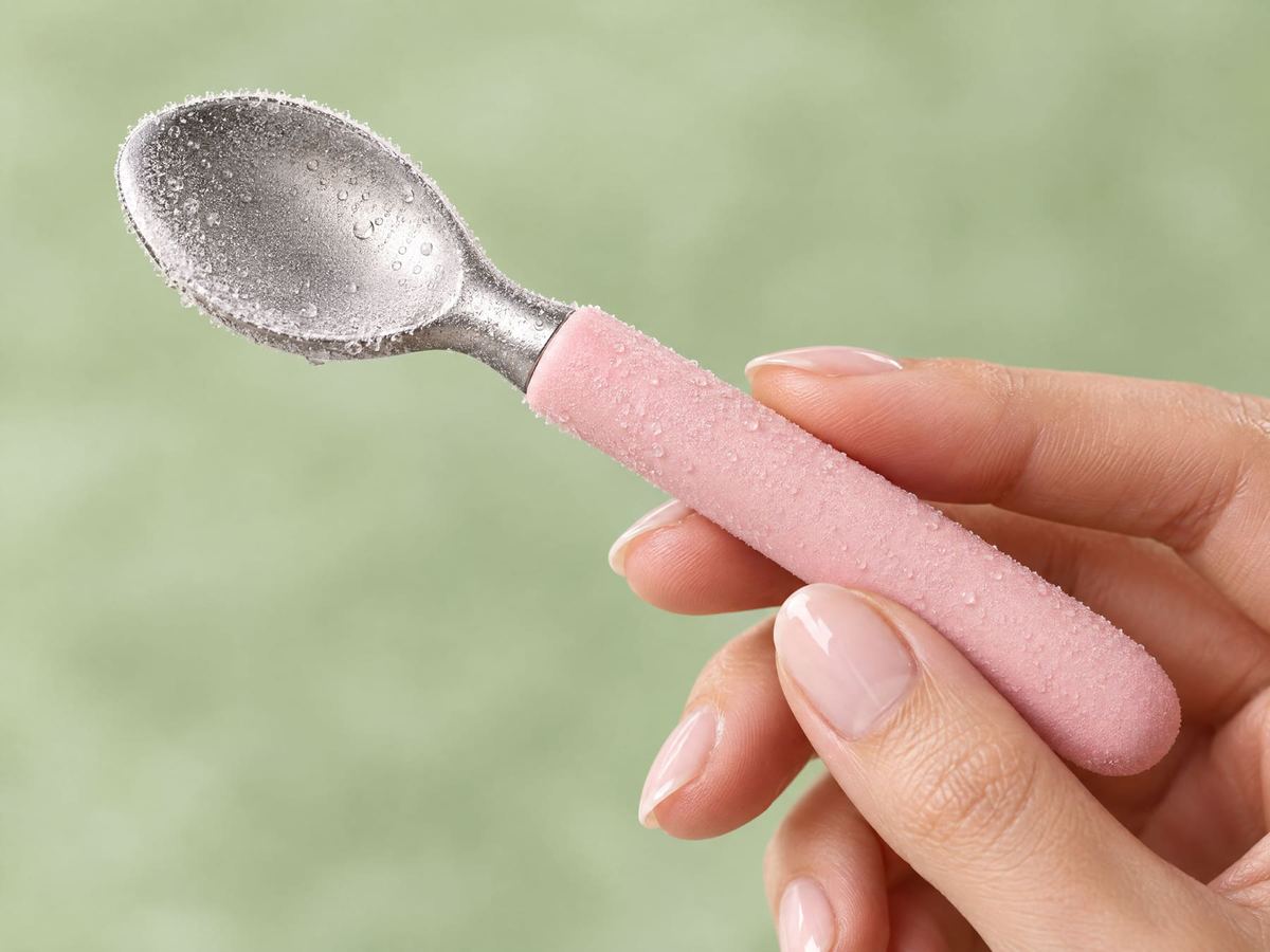 A hand holding the frosted gelo face roller, shaped like a gelato spoon with a pink handle.